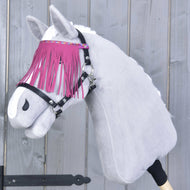 Hobby Horse en peluche de Hobby Horse LarDen portant le Licol noir avec franges roses, devant un fond en bois gris, avec robe blanche et têtière élégante à franges roses.