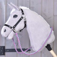 Rênes tricotées rose et bleu de Hobby Horse LarDen sur un Hobby Horse gris en peluche avec bride noire et rênes tressées à la main roses, bleues et blanches, monté sur un bâton en bois, sur un fond en bois clair.