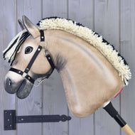 Hobby Horse Ozzy avec licol noir de Hobby Horse LarDen, avec visage beige en peluche, crinière en fil crème et noir, monté sur un bâton en bois, présenté sur fond de bois gris.