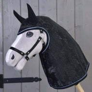 A stuffed toy horse head on a wooden stick wears the Hobby Horse LarDen Raincoat Silver Stone with ear covers and a halter, standing in front of a wooden paneled door.