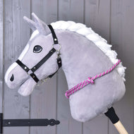Cordéo rayé rose de Hobby Horse LarDen, avec tête de cheval grise en peluche, crinière blanche, bride noire et cordéo rose et blanc sur un bâton en bois, idéal pour s’entraîner à monter sans bride devant un mur en bois gris.