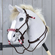 Hobby Horse gris avec tête en peluche, crinière blanche et yeux foncés portant la bride et le licol Ensemble de corde York de Hobby Horse LarDen avec accents rouges et blancs, devant un fond en bois gris.