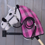Hobby Horse LarDen « Ensemble Harmonie Rose », jouet sur bâton gris fixé à un mur en bois, habillé d’une couverture d’écurie rose et noire à carreaux avec un licol noir et une longe assortie enroulée sur le côté.