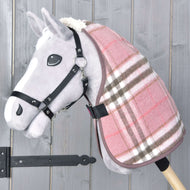 Couverture d'écurie Lady de Hobby Horse LarDen, sur un Hobby Horse gris en peluche avec couverture à carreaux roses et bruns et bride noire sur un bâton en bois, présenté devant un fond en bois gris.