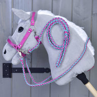 Ensemble Combinaison Parfaite Rose de Hobby Horse LarDen sur un Hobby Horse en peluche gris avec licol et rênes rose et turquoise rembourrés de fourrure, suspendu à un crochet mural sur fond de bois gris.