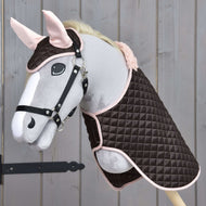 L’Ensemble Thermo Douceur de Hobby Horse LarDen présente un Hobby Horse en peluche avec bride, habillé d’un ensemble couverture matelassée marron et rose avec bonnet d’oreilles assorti, présenté sur fond en bois.