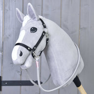 Rênes Tizian de Hobby Horse LarDen sur un Hobby Horse gris en peluche avec bride noire et rênes faites main, monté sur un bâton en bois devant un fond en panneaux de bois clair.