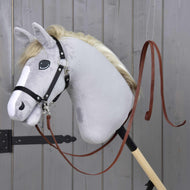 Hobby horse gris en peluche de Hobby Horse LarDen avec bride noire et Rênes Western Fendues Marron Foncé, monté sur un bâton en bois, sur fond de mur en bois gris.