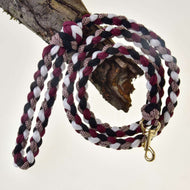 The Hobby Horse LarDen braided lead rope in black, white, and bordeaux hangs coiled over a tree branch, featuring a gold metal clasp at one end.
