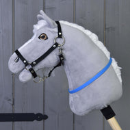 Hobby Horse cordeo bleu (taille S) de Hobby Horse LarDen, avec corps en peluche gris, crinière blanche, bride noire et ruban bleu-violet sur un bâton en bois, présenté devant un mur en bois gris.