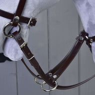 Gros plan de la Martingale marron de Hobby Horse LarDen, avec bride marron en cuir, boucles et anneaux métalliques sur une tête de cheval modèle gris clair, sur fond en bois gris.