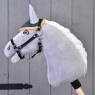 Hobby Horse LarDen en peluche grise avec crinière blanche, bride noire et bonnet d'oreilles Thermo Sport vert et jaune, sur un bâton en bois devant un mur en bois gris.
