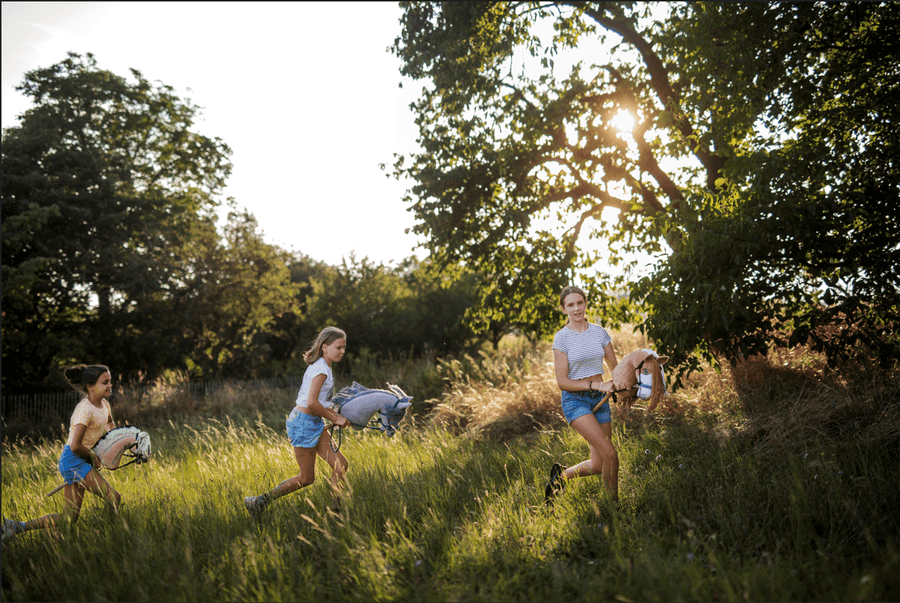 Children running with Hobby Horses through a sunny grassy field
