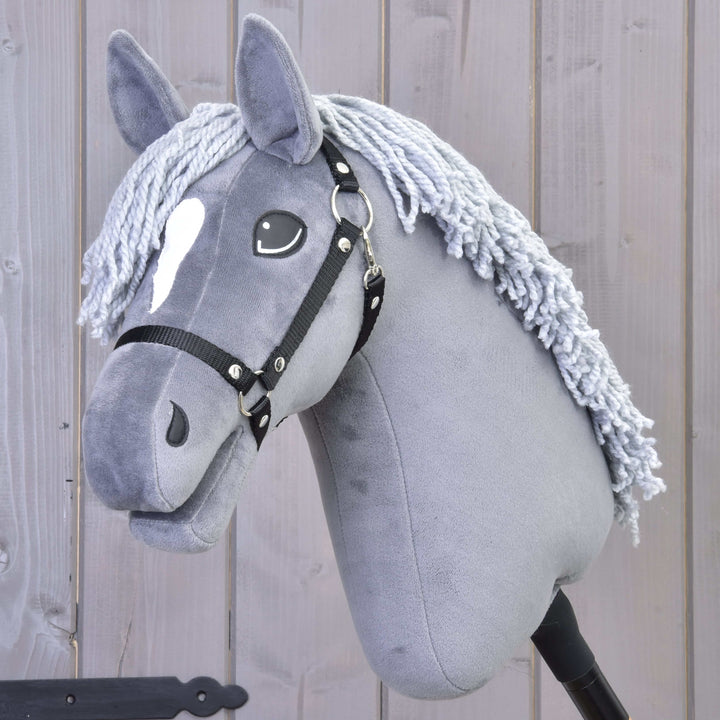 Hobby Horse gris avec une tache blanche sur le front, une bride noire et une crinière en fil, sur fond en bois.