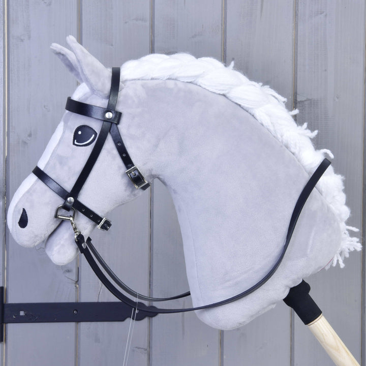 Bride complète noire en similicuir LarDen pour Hobby Horse avec longues rênes, sur un cheval en peluche gris clair à crinière blanche tressée