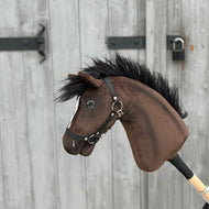 Hobby Horse Lucas avec licol noir de Hobby Horse LarDen, présenté devant une porte en bois grise avec charnières et loquet en métal noir.