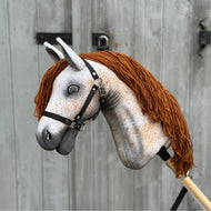 Hobby Horse Pompo avec licol noir de Hobby Horse LarDen, avec visage gris tacheté, crinière en fil marron et bride noire, inspiré de l'étalon hanovrien, présenté devant une clôture en bois patinée.