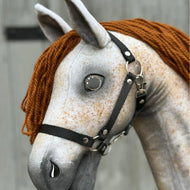 Gros plan sur Pompo de Hobby Horse LarDen montrant son corps gris fait main, ses yeux en bouton, sa crinière en fil marron et son licol noir, capturant l'allure joueuse d'un cheval hanovrien sur fond en bois flou.