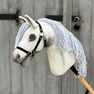 Hobby Horse Atlas avec licol noir de Hobby Horse LarDen, avec tête artisanale en tissu blanc, museau gris, licol noir et longue crinière en fil blanc, présenté devant une porte en bois patinée avec charnières en métal noir.