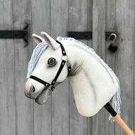 Hobby Horse Atlas avec licol noir de Hobby Horse LarDen, avec design Appaloosa blanc et crinière en fil gris, devant une porte en bois fermée par un loquet métallique et un cadenas.