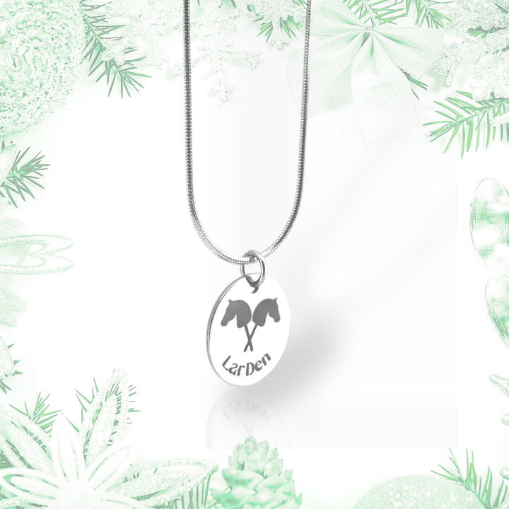 Collier avec pendentif Hobby Horse en acier inoxydable chirurgical de Hobby Horse LarDen, présenté sur un fond festif vert pâle et blanc avec branches de pin, nœuds et ornements.