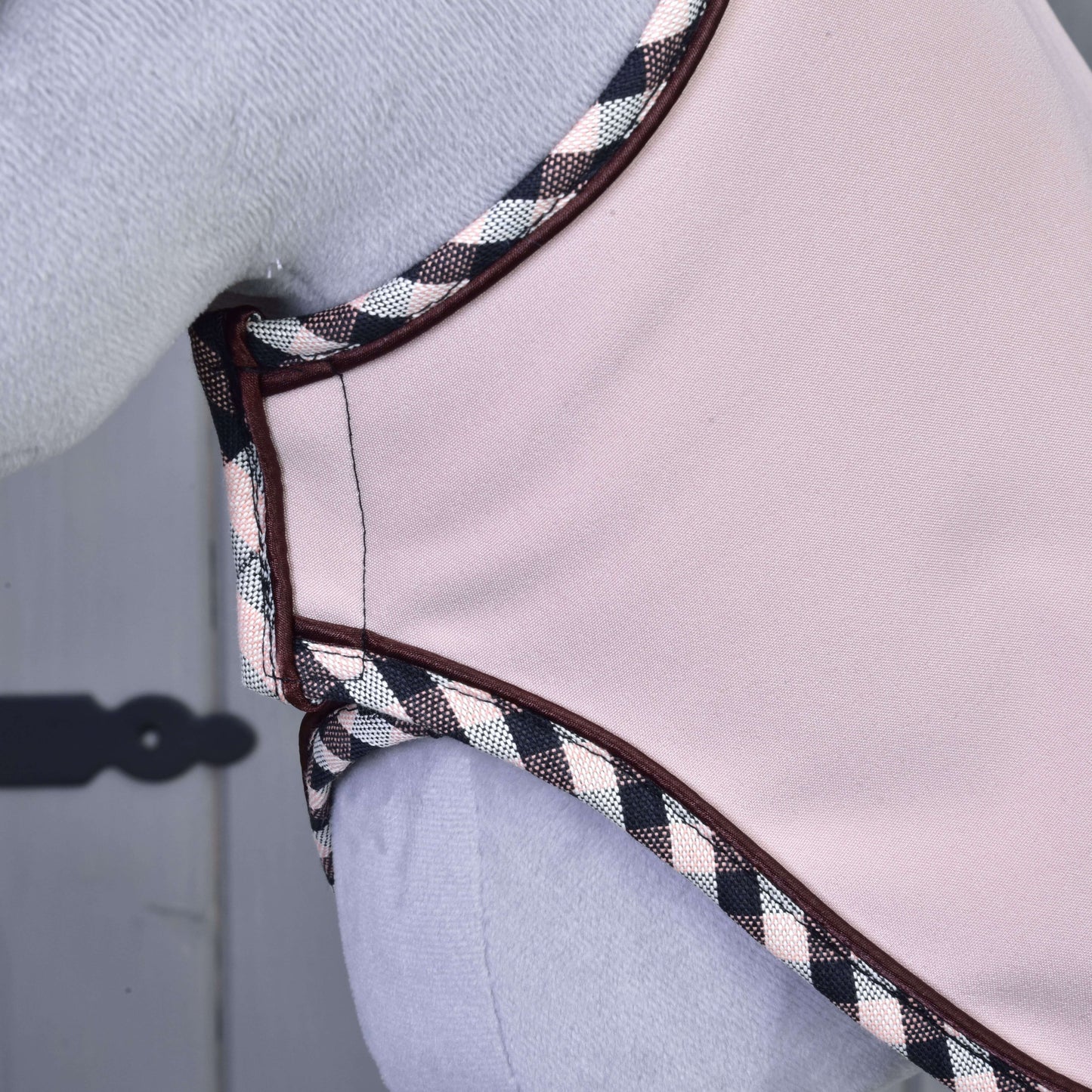 Gros plan sur l’Ensemble Abby de Hobby Horse LarDen, vêtement rose clair avec bordure à carreaux noirs, blancs et roses, semblable à un bonnet d’oreilles, porté sur fond clair avec une charnière décorative visible à gauche.