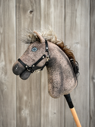 A close-up of the Hobby Horse LarDen "Hobby Horse Bolero with Black Halter" (size S), featuring a brown Appaloosa design, blue eye, fluffy mane, and set against a wooden plank background.