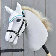 Gros plan sur un Hobby Horse en peluche gris de Hobby Horse LarDen avec crinière blanche, bride noire et Ear bonnet Glitter Cuties pour la protection contre les mouches, monté sur un bâton en bois devant une clôture en bois.