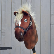 Hobby Horse Cinnamon avec Licol noir - taille S de Hobby Horse LarDen, en peluche marron avec liste blanche, licol noir et crinière blonde duveteuse, monté sur un bâton en bois devant une clôture en bois grise.