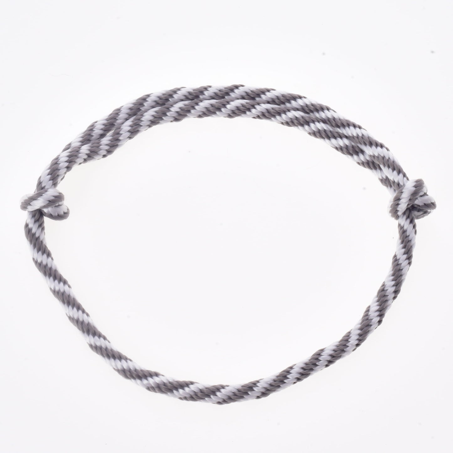 Une corde torsadée grise et blanche, formant un cercle avec des nœuds simples à chaque extrémité et présentée sur un fond blanc uni, fait partie de l’Ensemble Départ Argent (licol + cordelette + longe + rênes) de Hobby Horse LarDen, idéale comme rênes ou comme accessoire de licol et de longe pour votre Hobby Horse.