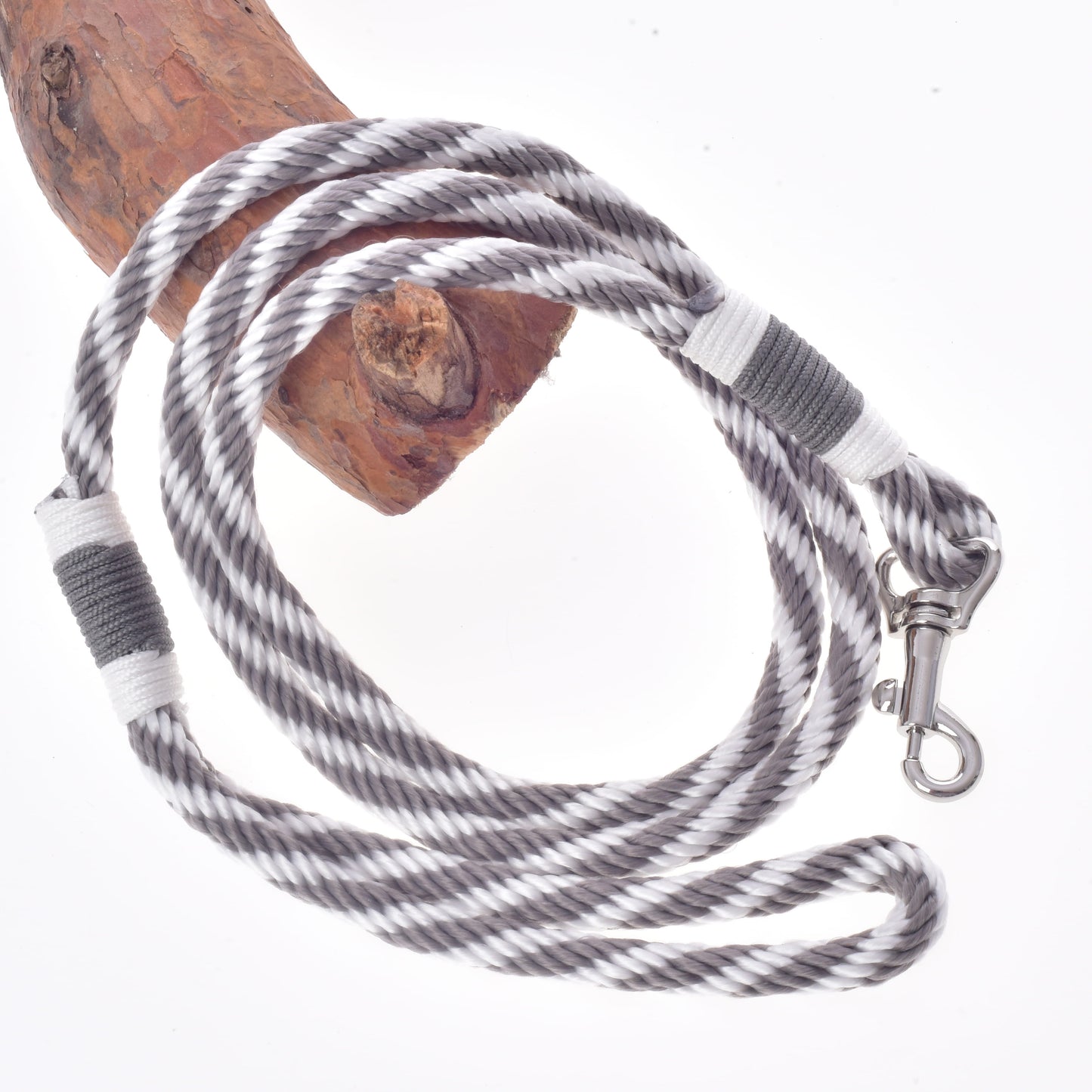 L’Ensemble Départ Argent de Hobby Horse LarDen, comprenant une longe enroulée rayée noir et blanc avec un clip métallique, repose partiellement enroulé autour d’une branche en bois sur un fond blanc, idéal comme rênes, licol ou longe avec vos accessoires Hobby Horse.