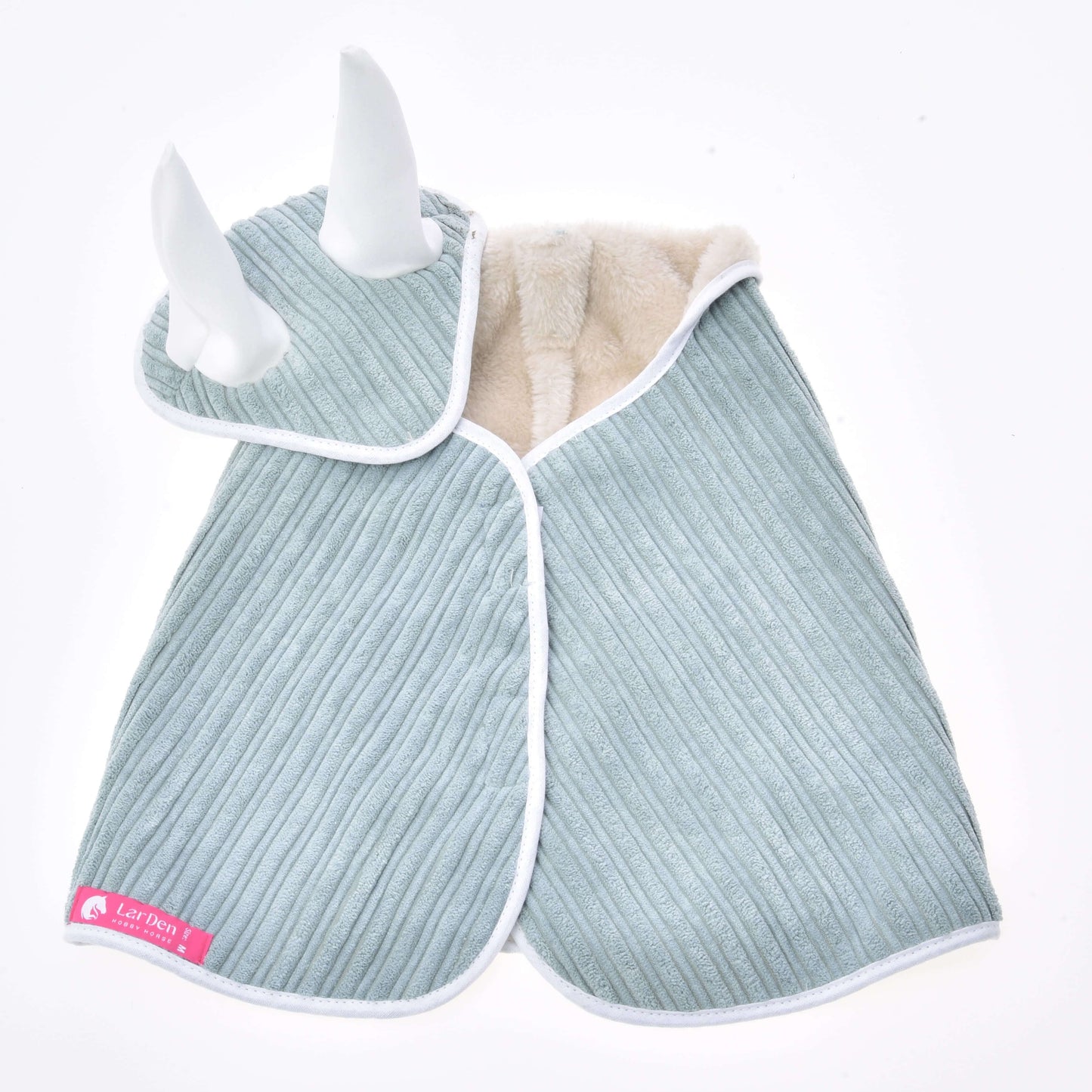 The Set Manchester Little Green by Hobby Horse LarDen is a ribbed, light blue pet cape with white trim and soft white horns on the hood, lined with beige fleece and finished with a pink Lil Pets tag—perfect for pairing with any blanket set or bonnet.