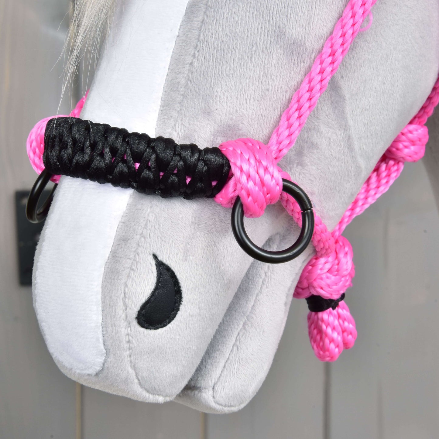 Gros plan sur le visage d’un cheval en peluche gris portant le Licou en corde Rose de Hobby Horse LarDen, avec corde rose vif, nœuds noirs et roses, anneaux métalliques et naseau noir cousu.