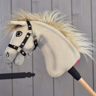 Hobby Horse Ivory Dream avec Licol noir - taille XS de Hobby Horse LarDen, avec fourrure ivoire douce et bâton en bois, appuyé contre un mur en bois gris.