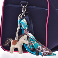 Gros plan sur un sac bleu marine à bordure rose, avec le Porte-clés Horse Grey de Hobby Horse LarDen et une écharpe colorée à motif nouée en nœud à l’un des anneaux métalliques du sac.