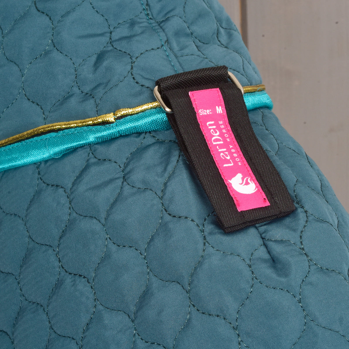 Gros plan sur la couverture Hobby Horse verte matelassée avec bordure turquoise et étiquette d’attache LarDen