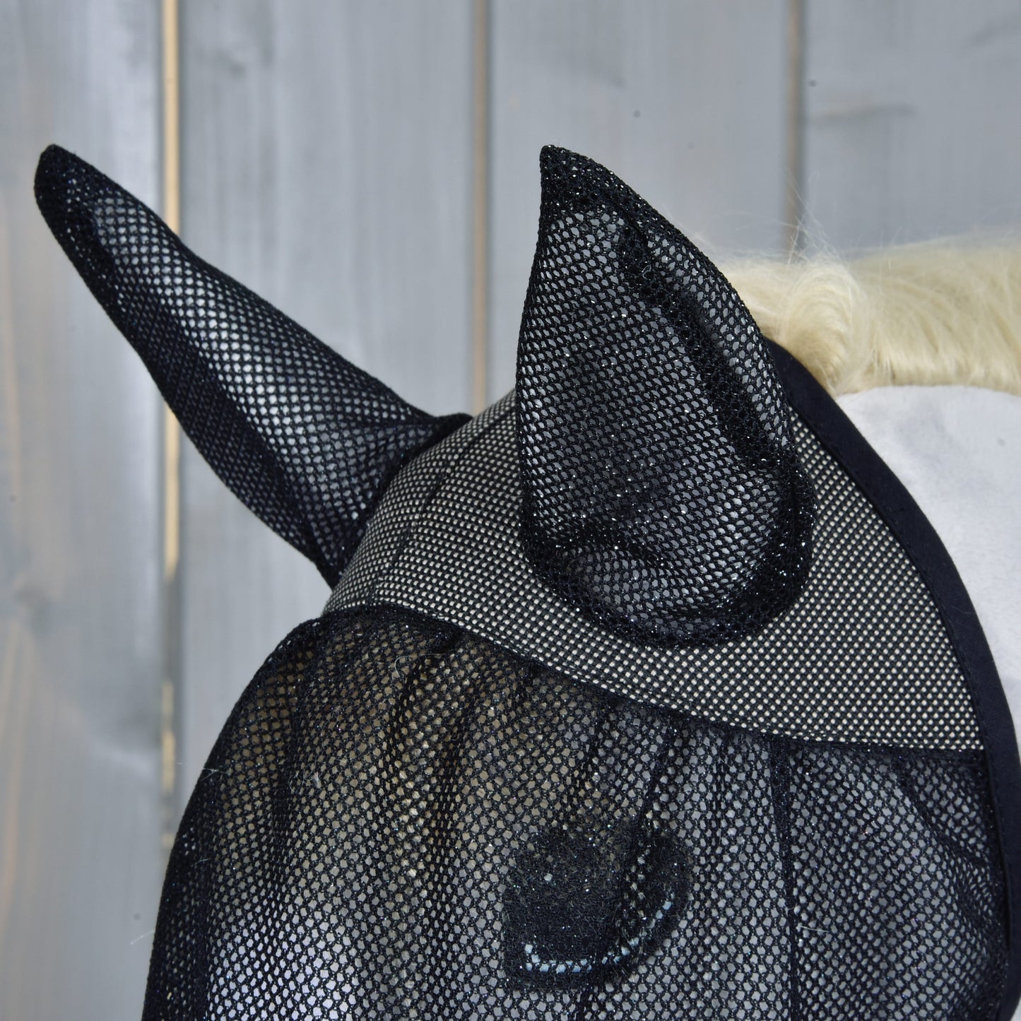 Gros plan sur une tête de cheval portant le Masque anti-mouches De Luxe complet de Hobby Horse LarDen pour la protection, avec un mur en bois en arrière-plan.