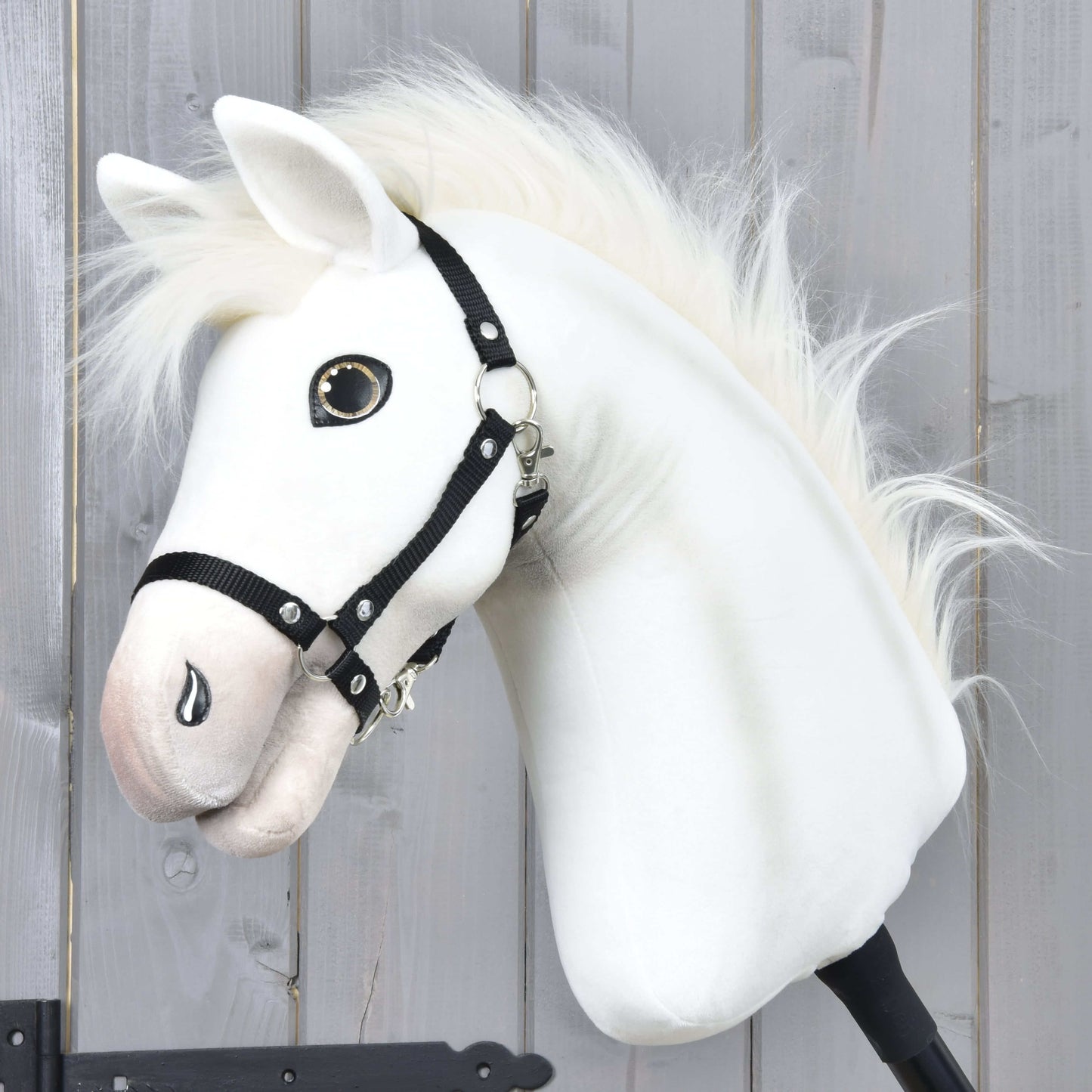 The Hobby Horse Nexus with Black Halter by Hobby Horse LarDen features a white plush Akhal-Teke-inspired head with button eye and fluffy mane, displayed against a wood wall—perfect for any Hobby Horse Nexus enthusiast.