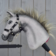 Hobby Horse Prestige avec Licol noir, taille XS de Hobby Horse LarDen, tête de hobby horse grise en peluche inspirée de l’élégance d’un cheval de sport Warmblood anglais. Il présente un visage expressif brodé, une crinière sauvage et un licol noir sécurisé, monté sur une poignée en bois. Posé sur un fond en bois, il est idéal comme support pour des aventures imaginatives de saut d’obstacles.