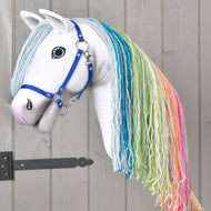 The Hobby Horse Rainbow New by Hobby Horse LarDen features a white body, a long yarn-based rainbow mane, and a blue halter for a fairy-tale look. Shown against gray wood-paneled siding with a black metal hinge on the left, this charming toy captures the imagination.