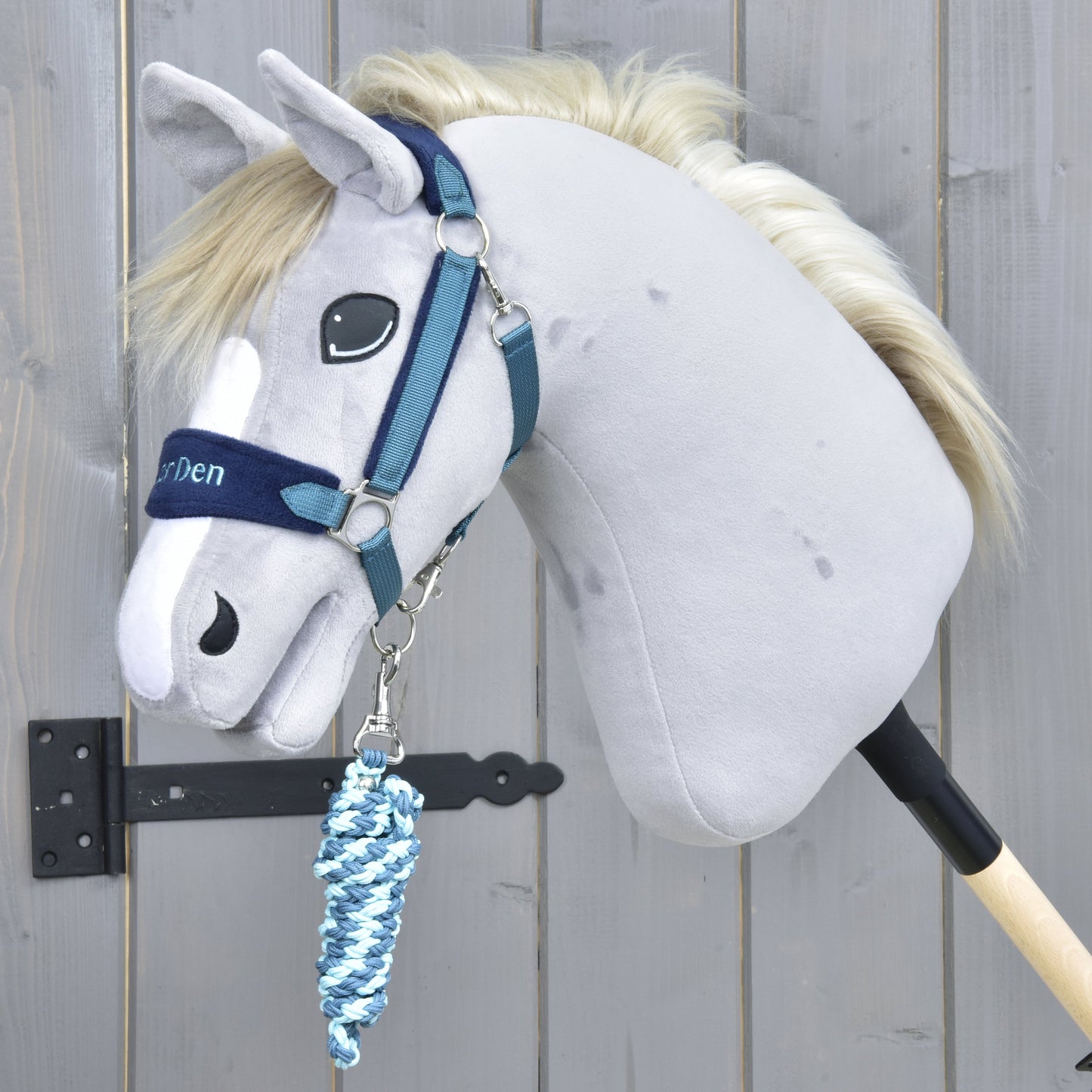 The Hobby Horse LarDen Set LarDen Exclusive Blue features a gray hobby horse with a blue halter and coiled blue-and-white lead rope, mounted on a wooden stick and shown against a wooden fence background.