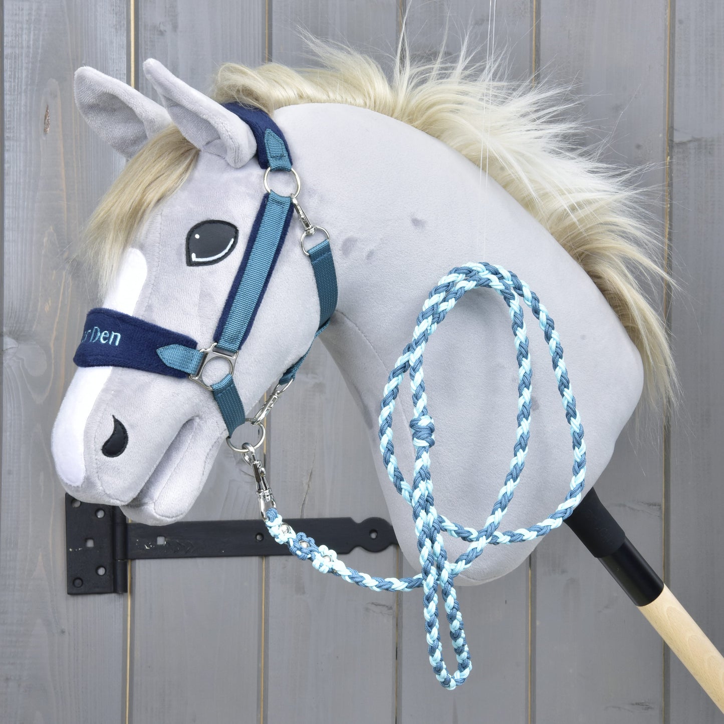 The Hobby Horse LarDen Set LarDen Exclusive Blue is a plush hobby horse stick toy with a light gray face, blue halter with fleece noseband, and braided lead rope, shown against a wooden background.