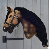 A plush brown Hobby Horse LarDen "Hobby Horse Stormy with Black Halter," featuring a black yarn mane, is mounted on a metal bracket against a wooden wall.