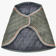 The Blanket Sport by Hobby Horse LarDen is a quilted, dark green dog coat with grey trim and light orange piping, inspired by protective horse blankets. Shown open and flat, it displays a diamond-stitched pattern and curved edges.