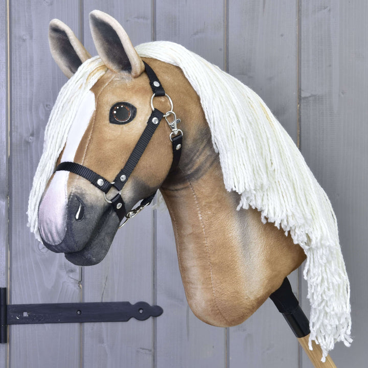 Hobby Horse Connie avec licol noir de Hobby Horse LarDen, avec design réaliste beige et blanc, longue crinière en fil blanc, présenté monté sur un bâton devant un mur en bois gris.