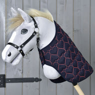 Hobby Horse en peluche avec licol noir et couverture matelassée pour Hobby Horse Blanket Pink Heart de Hobby Horse LarDen, décorée de cœurs roses, posé sur fond en bois.