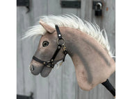 Hobby Horse Happy Boy avec licol noir de Hobby Horse LarDen, avec allure réaliste de hanovrien brun clair, crinière blanche, licol noir et yeux expressifs, présenté devant une porte en bois grise avec détails en métal noir.