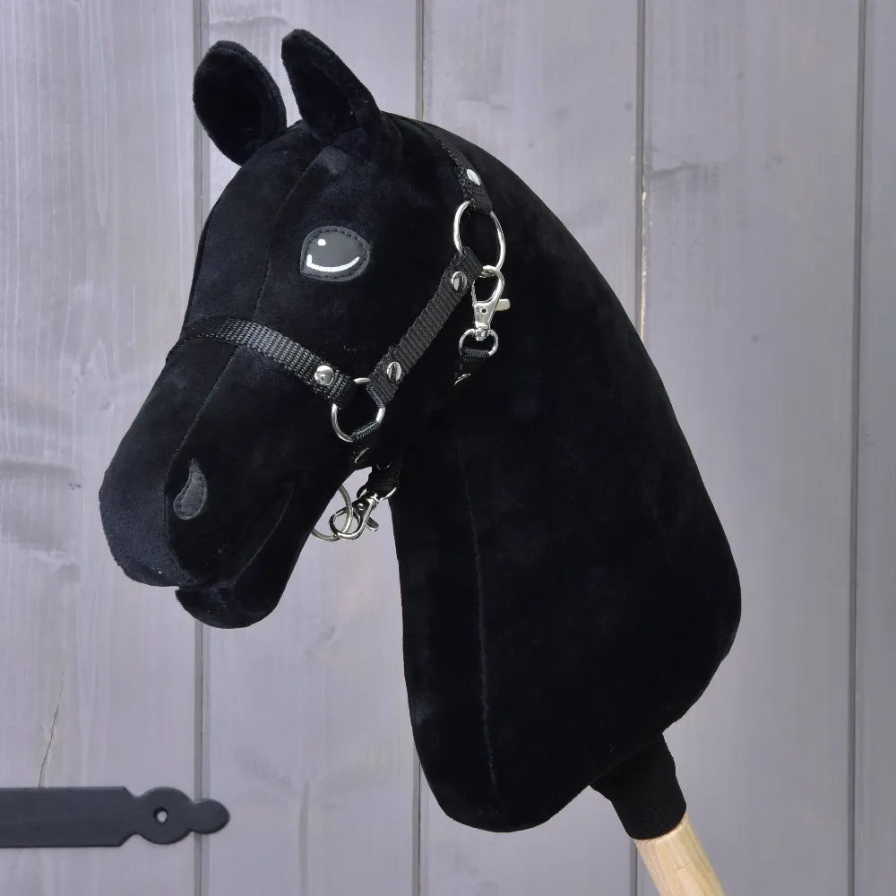 Construis ton cheval, tête pour Hobby Horse personnalisée en peluche noire avec crinière tricolore en fausse fourrure, bride et rênes sur un bâton en bois, devant un panneau en bois gris, à personnaliser comme vous le souhaitez.