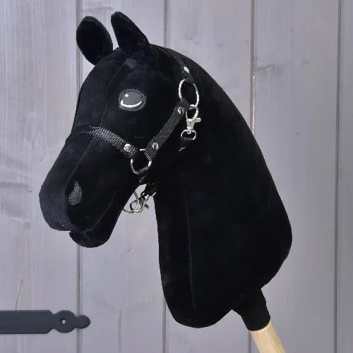 Construis ton cheval, tête noire faite main pour Hobby Horse, avec bride et montée sur un bâton en bois, présentée devant un mur en bois gris.