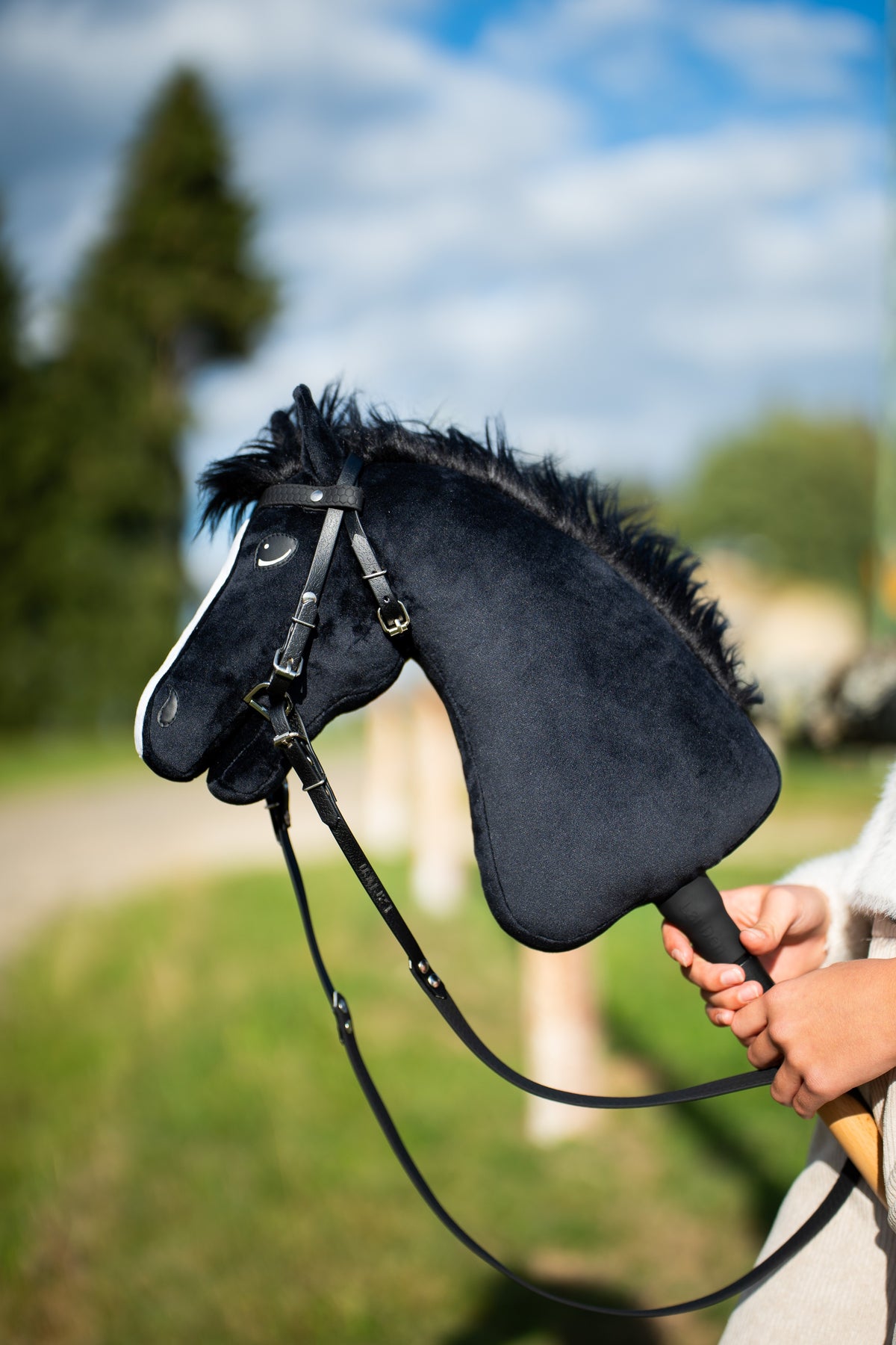Black Hobby Horse wearing a black leatherette bridle with reins outdoors